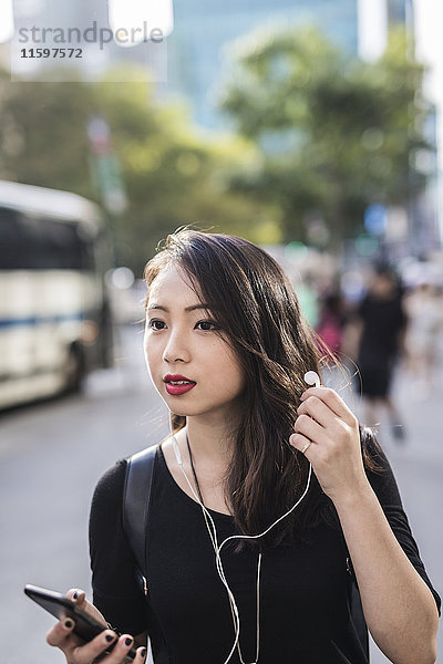 Porträt einer jungen Frau mit Kopfhörer und Handy  die etwas sieht.