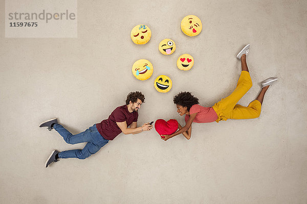 Glückliche Paare  die auf ihren Smartphones SMS schreiben und Emojies verschicken.