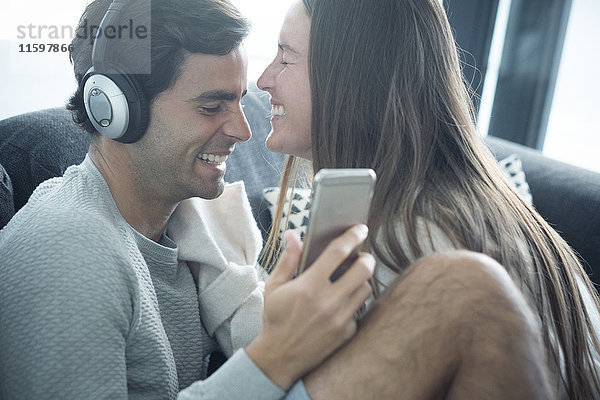 Glückliches junges Paar mit Kopfhörer und Smartphone zu Hause