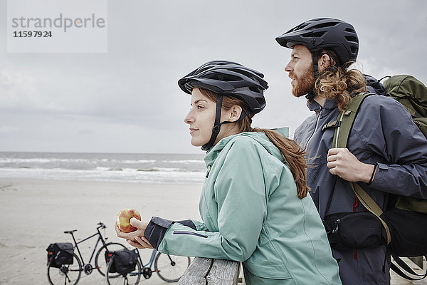 Deutschland  Schleswig-Holstein  St. Peter-Ording  Paar auf einer Fahrradtour mit Pause am Steg am Strand