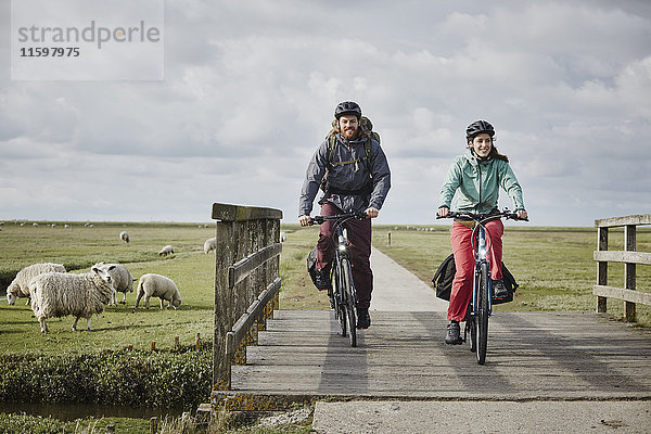 Deutschland  Schleswig-Holstein  Eiderstedt  Paar auf Fahrrädern über die Brücke auf dem Weg durch Salzwiesen