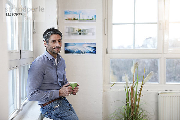 Porträt des lächelnden Mannes mit Tasse Kaffee im Büro