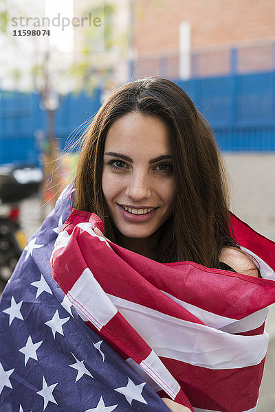Porträt einer lächelnden jungen Frau in US-amerikanische Flagge gehüllt