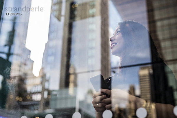 USA  New York City  Manhattan  lächelnde junge Frau hinter Glasscheibe schaut nach oben