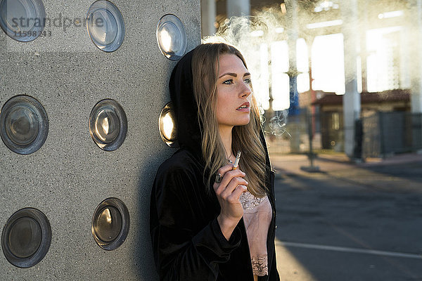 Porträt einer blonden jungen Frau  die im Gegenlicht eine Zigarette raucht.