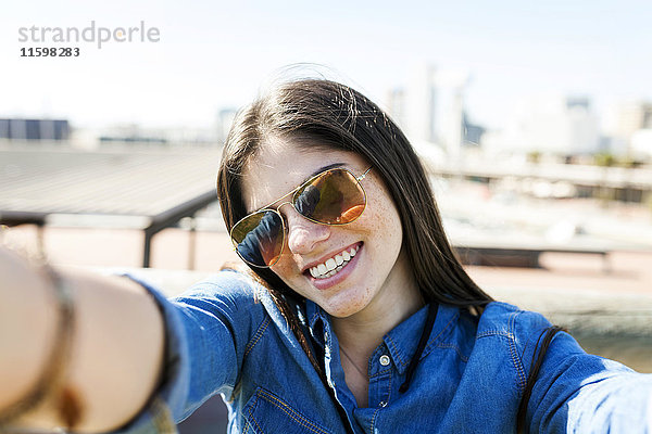 Porträt einer lächelnden jungen Frau mit Sonnenbrille  die sich selbst trägt.