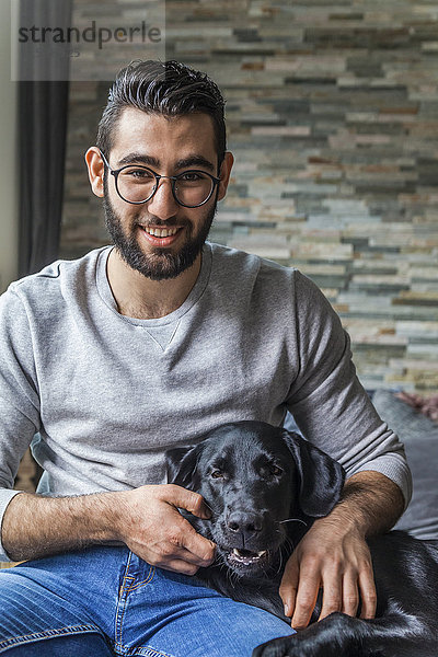 Porträt eines lächelnden jungen Mannes mit seinem Hund zu Hause