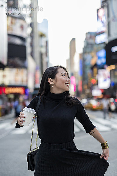 USA  New York City  Manhattan  junge Frau in schwarz gekleidet mit Kaffee  um auf die Straße zu gehen.