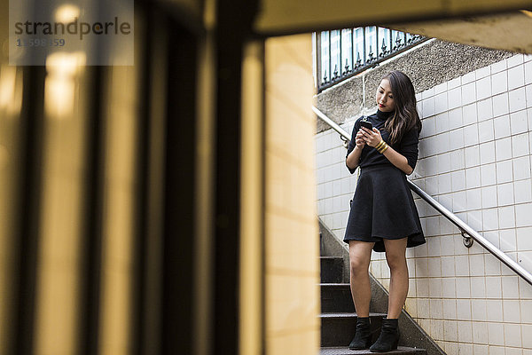 USA  New York City  Manhattan  junge Frau steht auf der Treppe und schaut auf das Smartphone.