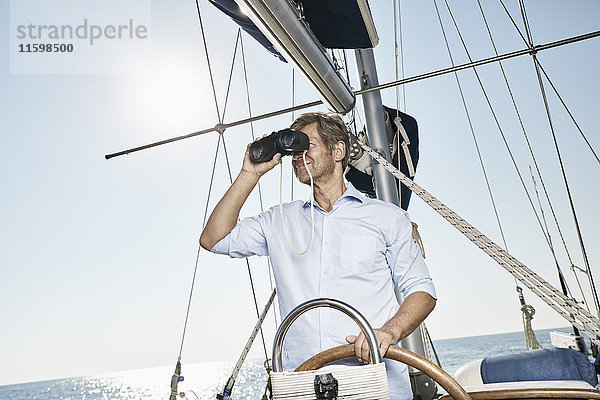 Erwachsener Mann mit Fernglas am Steuer seines Segelbootes