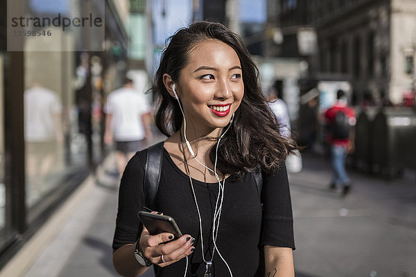USA  New York City  Manhattan  junge Frau beim Musikhören mit Handy und Kopfhörer auf der Straße