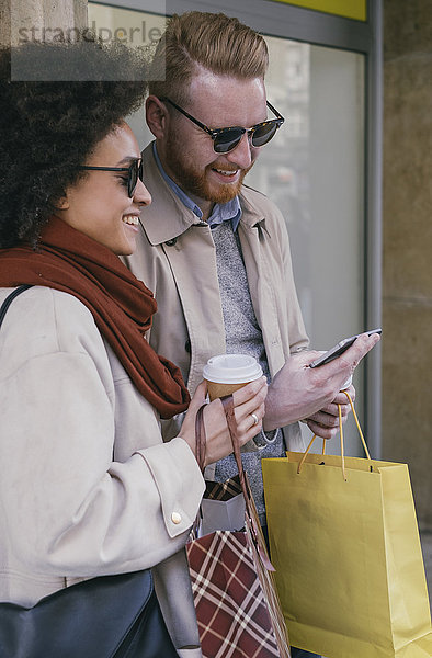 Glückliches Paar in der Stadt mit Handy und Einkaufstaschen