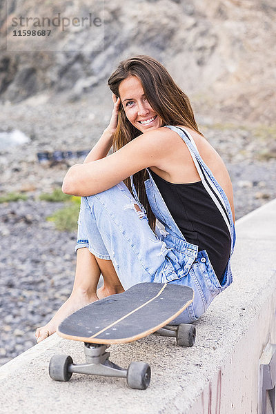 Porträt einer lächelnden Frau mit Skateboard auf einer Wand sitzend