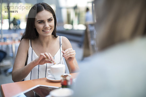 Lächelnde Frau  die einen Freund in einem Café im Freien ansieht.