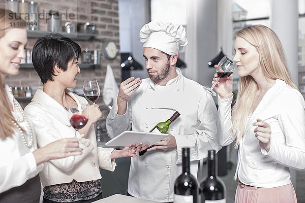 Chefkoch mit drei Frauen  die in der Küche Rotwein probieren