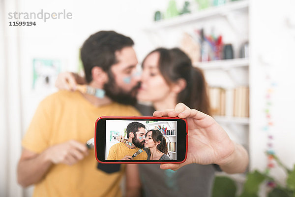 Junges Paar  das sich küsst und einen Selfie mit Pinseln nimmt.