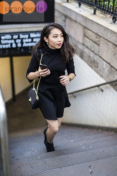 USA  New York City  Manhattan  junge Frau in schwarz gekleidet  die die Treppe hinaufgeht.