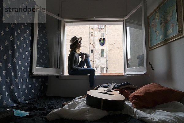 Junge Frau mit Hut im Fensterrahmen sitzend