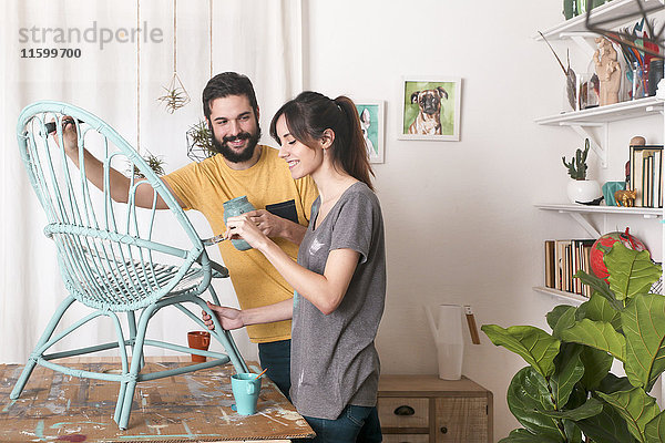 Junges Paar malt Korbsessel in blau zu Hause