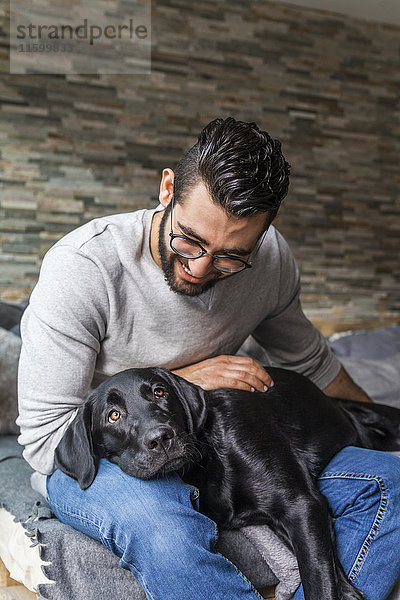 Lächelnder Mann mit seinem Hund auf der Couch zu Hause