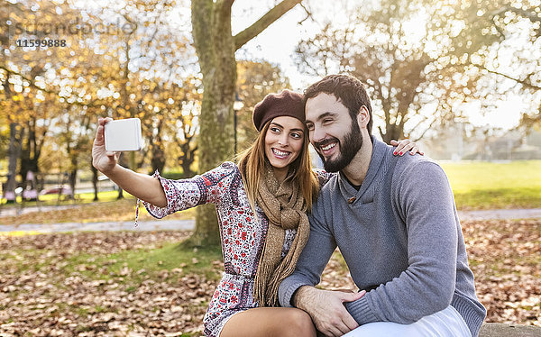Glückliches Paar nimmt Selfie mit Smartphone im herbstlichen Park