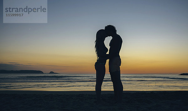 Junges Paar  das sich in der Abenddämmerung am Strand küsst.