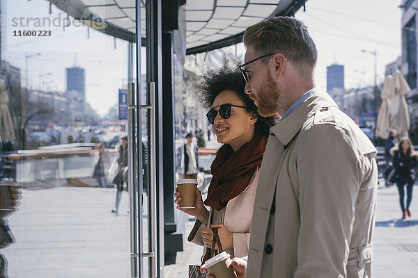 Paar in der Stadt mit Kaffee zum Mitnehmen im Schaufenster