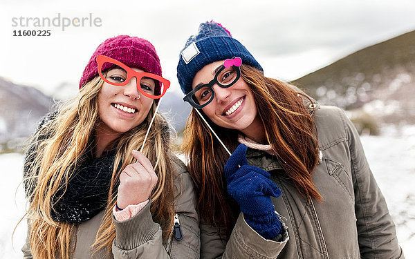 Zwei junge Frauen mit gefälschter Brille haben Spaß in den schneebedeckten Bergen