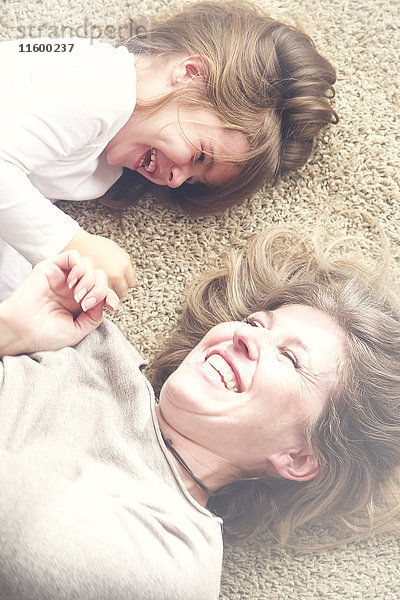 Mutter und Tochter liegen auf dem Teppich und haben Spaß.