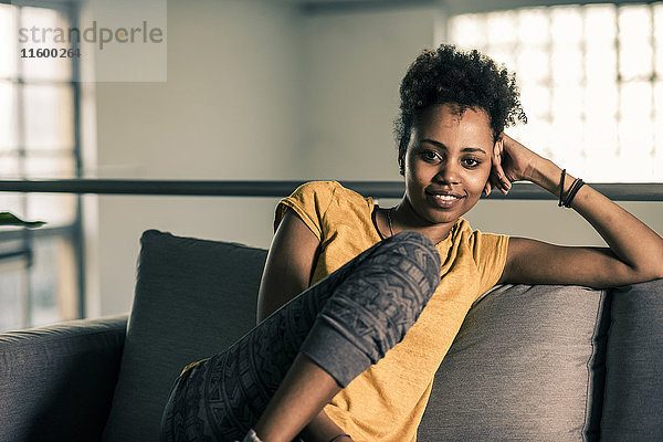 Porträt einer lächelnden jungen Frau  die auf der Couch sitzt.