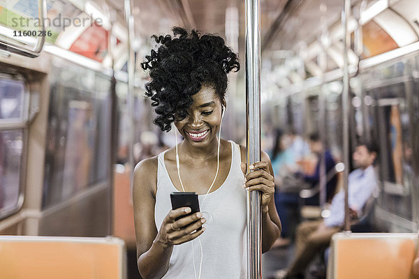 USA  New York City  Manhattan  Porträt einer glücklichen Frau beim Blick auf das Handy in der U-Bahn