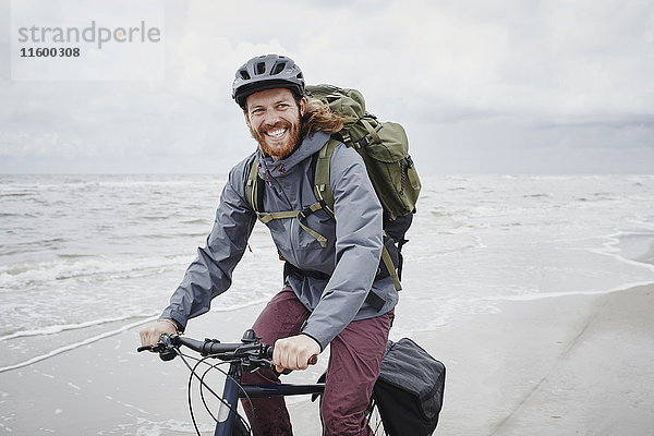 Deutschland  Schleswig-Holstein  St. Peter-Ording  glücklicher junger Mann auf dem Fahrrad am Strand
