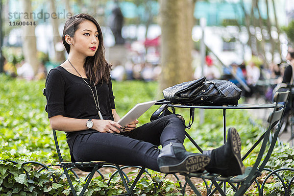 USA  New York  junge Frau mit Tablette im Stadtpark sitzend