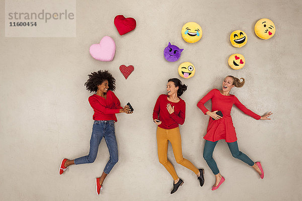Weibliche Freunde  die mit Emojies über ihren Köpfen plaudern und klatschen.