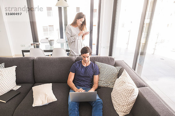 Junges Paar zu Hause mit Handy und Laptop