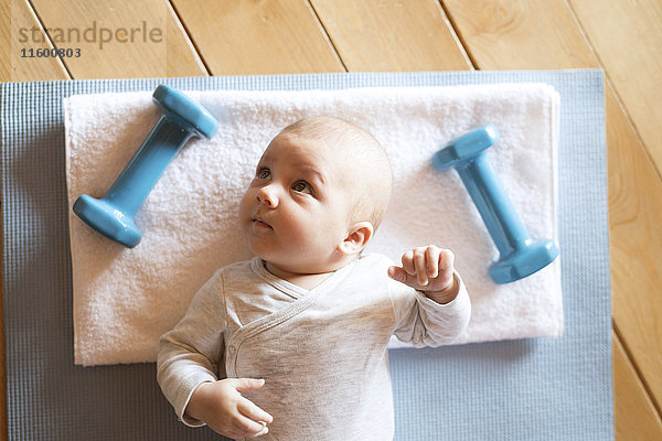 Baby zu Hause auf Matte neben Hanteln liegend