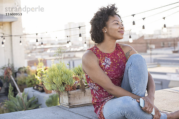 Junge Frau sitzt auf der Dachterrasse und genießt die Sonne.