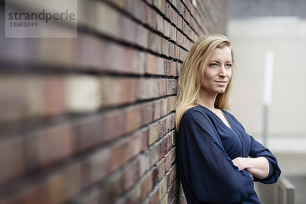 Porträt einer lächelnden  blonden jungen Frau  die sich an die Wand lehnt.