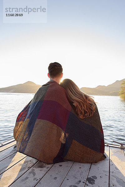 Paar sitzt auf einem Steg am Fluss  eingewickelt in eine Decke