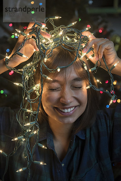 Mixed Race Frau hält Lichterkette auf dem Kopf in der Nähe von Weihnachtsbaum