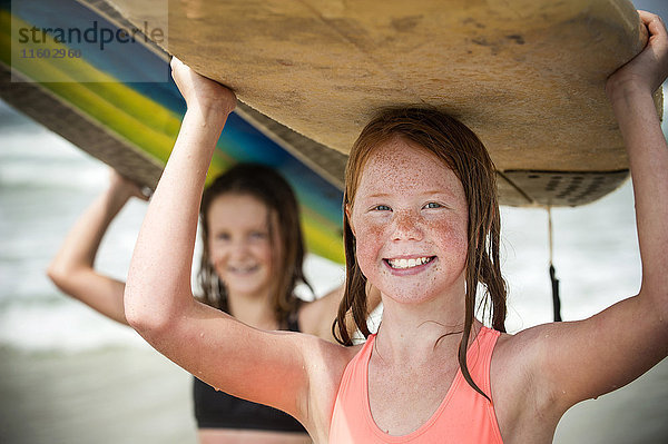 Porträt von lächelnden Mädchen  die Surfbretter auf ihren Köpfen balancieren