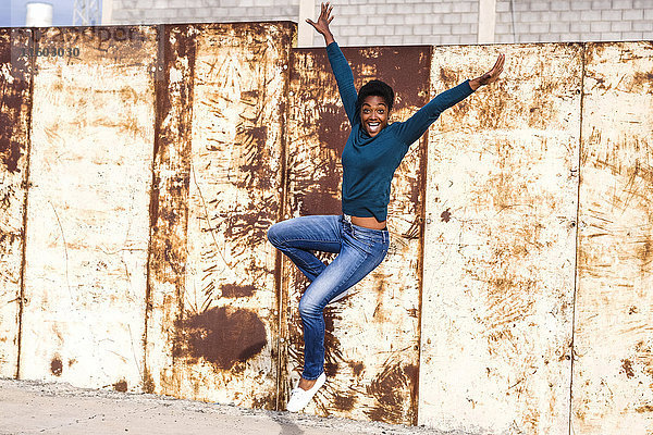 Vor Freude springende afroamerikanische Frau in der Nähe einer rostigen Metallwand