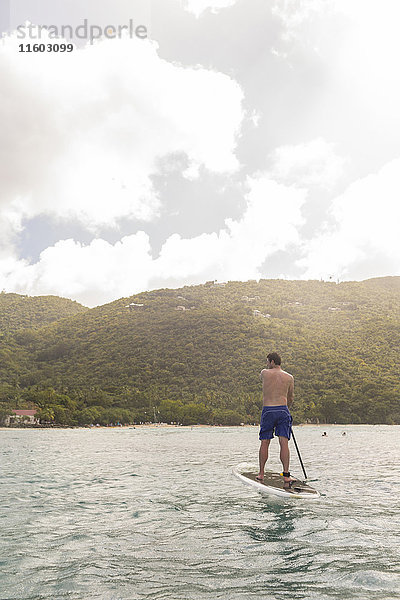Kaukasischer Mann steht auf einem Paddelbrett auf dem Meer