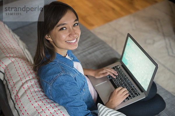 Lächelnde Mixed Race Frau mit Laptop auf dem Sofa