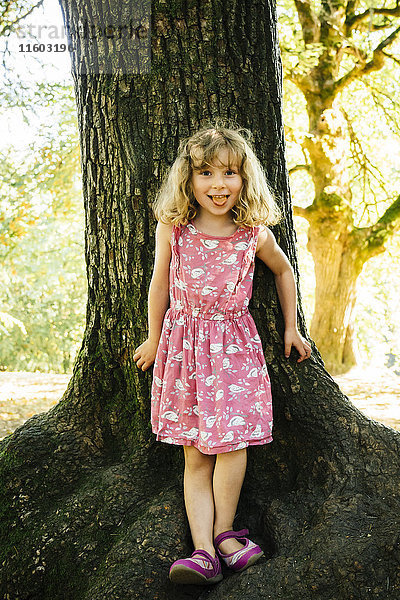 Porträt eines lächelnden kaukasischen Mädchens  das sich an einen Baum lehnt