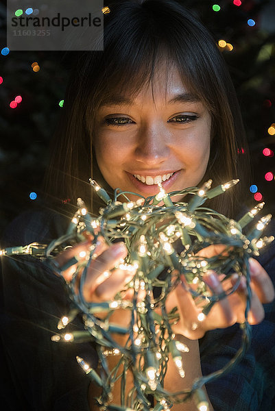 Mixed Race Frau hält Lichterkette in der Nähe von Weihnachtsbaum