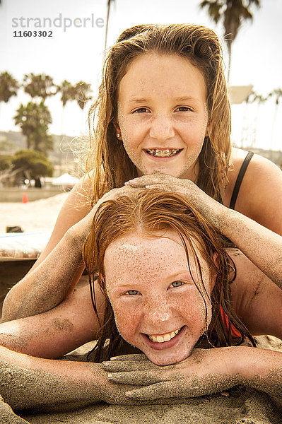 Porträt von lächelnden Mädchen  die am Strand liegen und mit Sand bedeckt sind