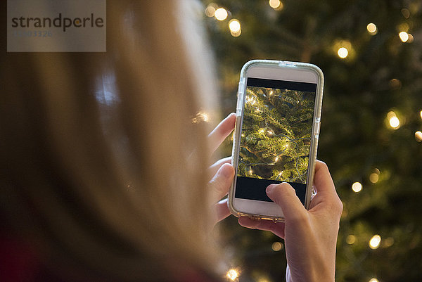 Kaukasische Frau fotografiert Weihnachtsbaum mit Mobiltelefon