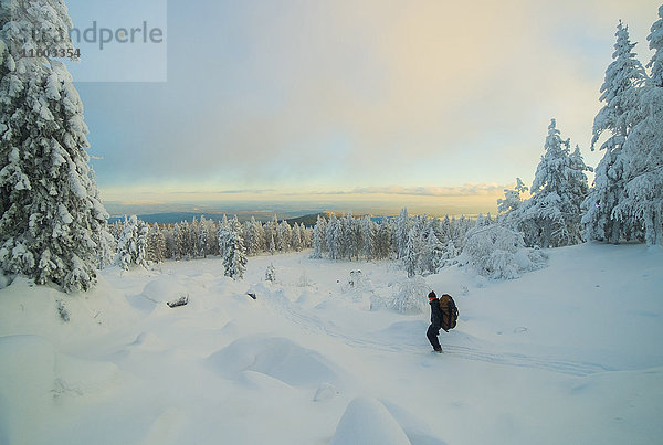 Kaukasischer Mann beim Wandern im verschneiten Wald bei Sonnenuntergang