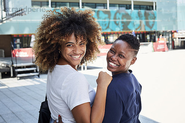 Porträt von lächelnden schwarzen Frauen  die sich in der Stadt umarmen